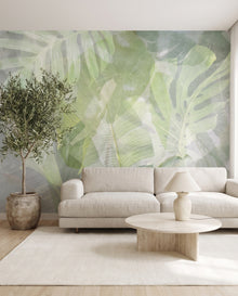 Papier peint panoramique feuillages Sève : monstera et bananier aquarelle vert tendre dans un salon lin avoine avec table en travertin, Wonderwall Casablanca