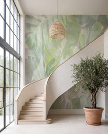 Papier peint panoramique Sève dans une orangerie double hauteur à escalier de plâtre et verrière acier : fresque botanique vert tendre Wonderwall Casablanca